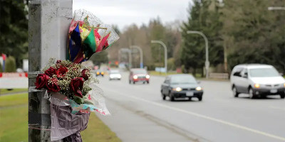 Bouquet de fleurs et roses accroché à un poteau en bord de route, avec des voitures circulant en arrière-plan, évoquant un hommage ou un mémorial routier.