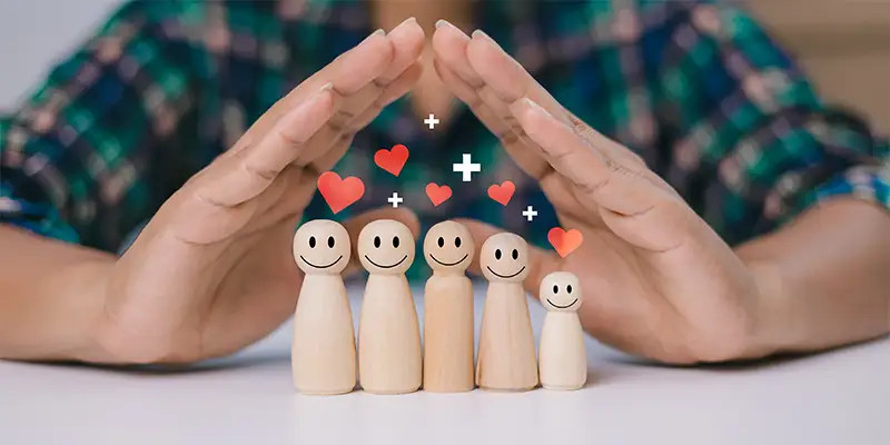 Mains formant un cœur au-dessus de figurines en bois souriantes de tailles différentes, symbolisant l'amour et la croissance familiale.