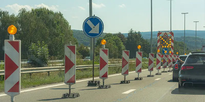 Chantier routier avec une déviation signalée par des cônes lumineux, des panneaux de signalisation temporaires et une barrière à bandes rouges et blanches, sous un ciel dégagé.